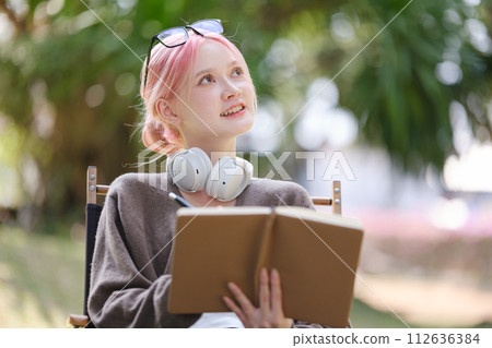 Young Happy Artist woman drawing book and wearing headphones in the garden. 112636384