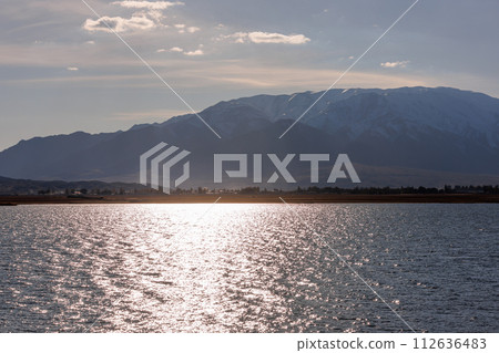 Blue calm water in Issyk-Kul lake with mountains on background at sunny autumn evening 112636483