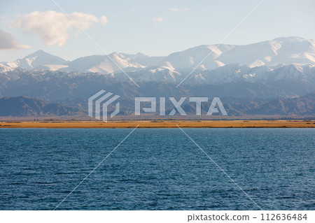 Blue calm water in Issyk-Kul lake with mountains on background at autumn afternoon 112636484