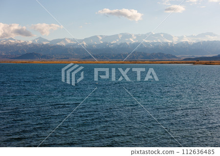 Blue calm water in Issyk-Kul lake with mountains on background at autumn afternoon 112636485