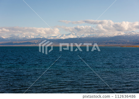 Blue calm water in Issyk-Kul lake with mountains on background at autumn afternoon 112636486