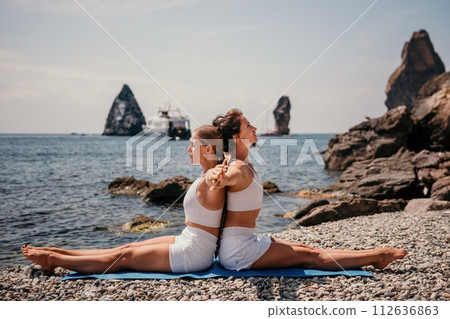 Woman sea yoga. Two Happy women meditating in yoga pose on the beach, ocean and rock mountains. Motivation and inspirational fit and exercising. Healthy lifestyle outdoors in nature, fitness concept. 112636863