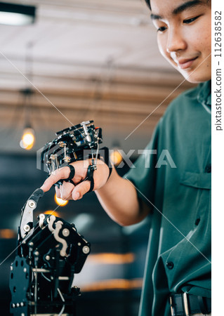 Teenage boy in a technical college learns technology testing a robot hand and arm touching fingers for educational skill growth. Embracing futuristic AI and humanity. Teenage boy in a technical college learns technology testing a robot hand and arm touching fingers for educational skill growth. Embracing futuristic AI and humanity. 112638582