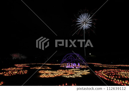 Candles lined up in Kairakuen at night during the Plum Festival and the bright fireworks that spread out beyond them 112639112