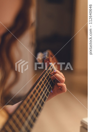 Close up of a teenage girl learning to playing acoustic guitar at home. Young girl playing music on guitar. 112640646