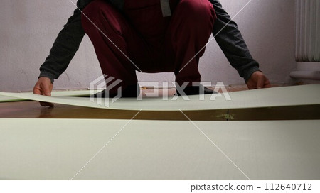 The employee man lays a bright soft substrate for floor insulation in the room, covering the floor with sheets of the substrate before laying the laminate 112640712