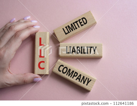 LLC - Limited liability company. Wooden cubes with word LLC. Businessman hand. Beautiful pink background. Business and LLC concept. Copy space. 112641186