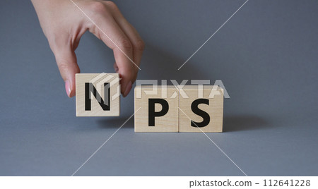NPS - Net Promoter Score symbol. Wooden cubes with words NPS. Businessman hand. Beautiful grey background. Business and NPS concept. Copy space. 112641228