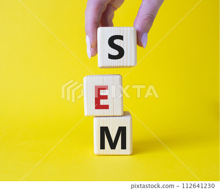 SEM - Search Engine Marketing symbol. Wooden cubes with words SEM. Businessman hand. Beautiful yellow background. Business and SEM concept. Copy space. SEM - Search Engine Marketing symbol. Wooden cubes with words SEM. Businessman hand. Beautiful yellow background. Business and SEM concept. Copy space. 112641230