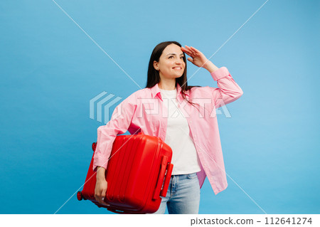 Portrait of happy young woman holding red suitcase isolated on blue background 112641274
