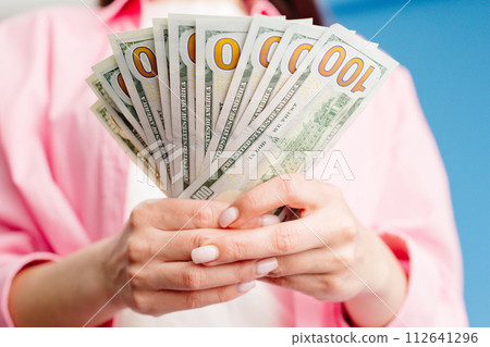 Close-up of female hands counting stack of hundred dollar bills blue background Close-up of female hands counting stack of hundred dollar bills blue background 112641296