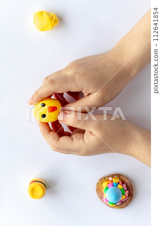 The hands of a small child are holding a yellow plasticine chicken. 112641854