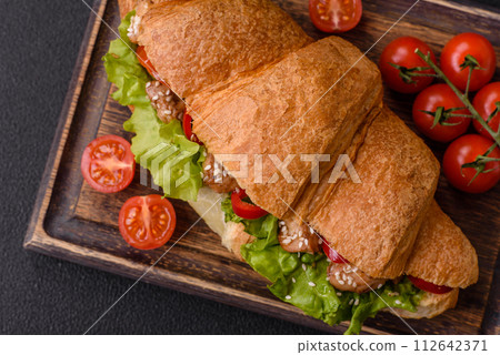 Delicious fresh crispy croissant with chicken or beef meat, lettuce, tomatoes, spices and sauce 112642371