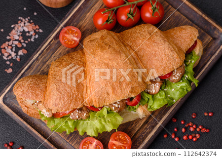 Delicious fresh crispy croissant with chicken or beef meat, lettuce, tomatoes, spices and sauce 112642374