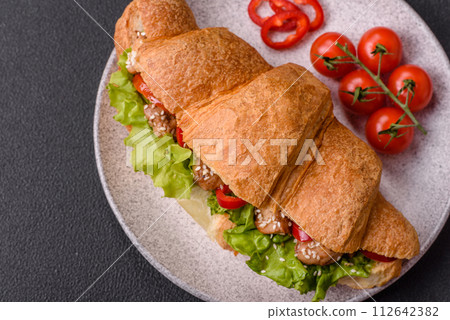 Delicious fresh crispy croissant with chicken or beef meat, lettuce, tomatoes, spices and sauce 112642382
