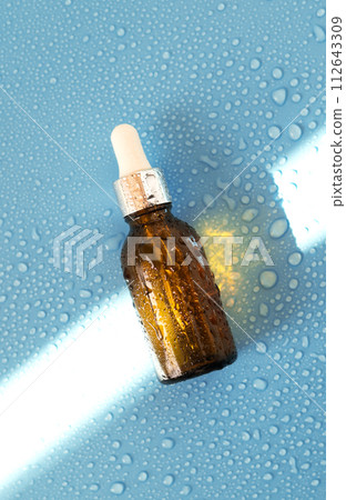 Serum bottle , oil cosmetic on blue background with hard light and water drops. with shadows flat lay, top view 112643309