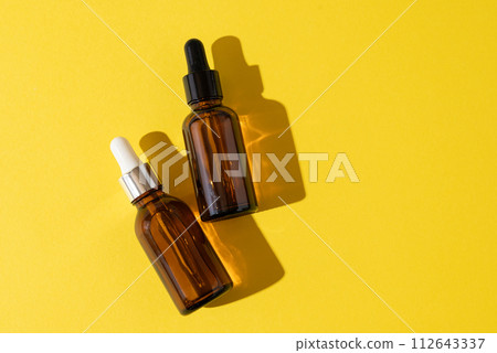 A glass bottles with a pipette with oil, serum brown on a yellow background. Flat Lay and hard light 112643337