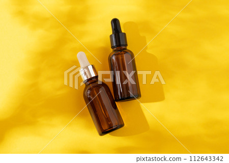 A glass bottles with a pipette with oil, serum brown on a yellow background. Flat Lay and hard light 112643342
