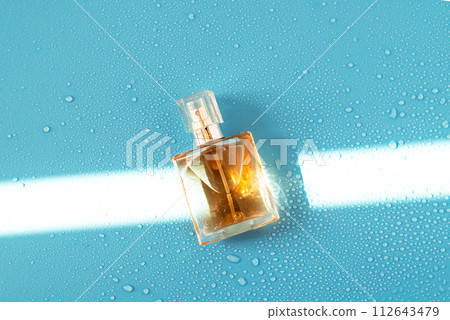 Perfume woman bottle on blue background with hard light and water drops. with shadows flat lay, top view 112643479