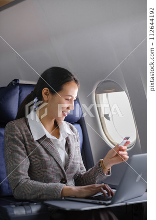 Asian female using laptop computer and holding credit card in airplane, Business traveling and technology concept. 112644192