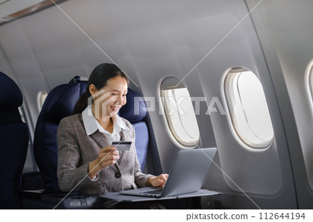 Asian female using laptop computer and holding credit card in airplane, Business traveling and technology concept. 112644194