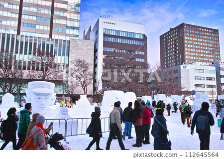 Sapporo Snow Festival with blue skies visible, tourists walking through Odori Park lined with small snow statues 112645564
