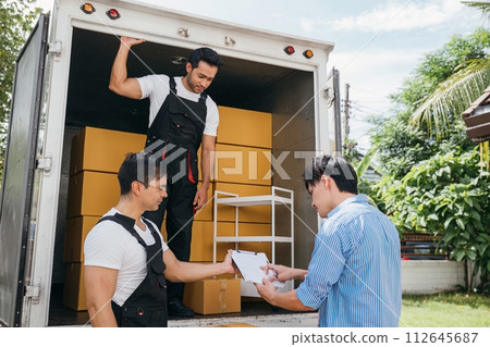 A couple pleased signs the delivery checklist after professional movers help with furniture lifting. Uniformed employees demonstrate teamwork for customer satisfaction. Moving Day Concept A couple pleased signs the delivery checklist after professional movers help with furniture lifting. Uniformed employees demonstrate teamwork for customer satisfaction. Moving Day Concept 112645687