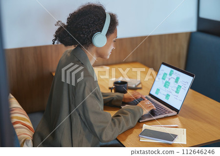 A woman with headphones using a laptop at a table in an office building 112646246