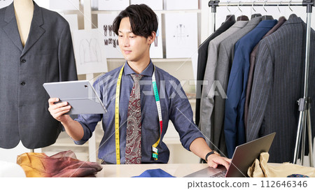 一位年輕的服裝設計師一邊看著平板電腦一邊工作 112646346