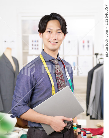 A young clothing designer looking at the camera while holding a laptop 112646357