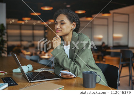 A woman is working on a laptop and cell phone at a table in nice modern coworking office 112646379