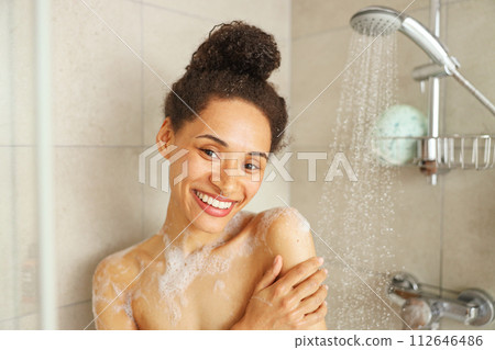 The woman is showering and smiling in the bathroom, enjoying the event 112646486