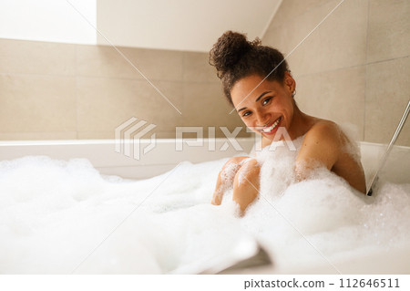 Woman happily bathes in foamfilled tub, smiling with comfort and relaxation Woman happily bathes in foamfilled tub, smiling with comfort and relaxation 112646511