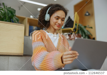 A happy woman with headphones smiles while using a tablet computer 112646537