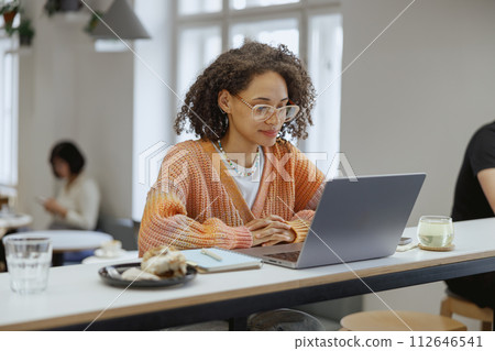 A woman is seated at a table, using a laptop computer A woman is seated at a table, using a laptop computer 112646541