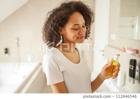 A happy woman holds a bottle of oil, smiling in the bathroom 112646546