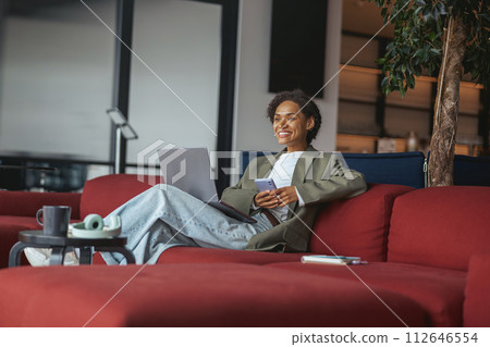 Woman on red couch in nice modern coworking office, using laptop and phone for leisure and comfort 112646554