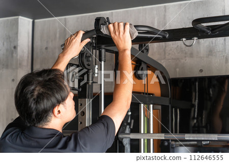 A man wiping a power rack with a towel after using it at a sports gym (manners, rules, infection control, alcohol disinfection) 112646555