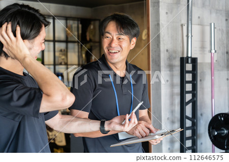 年輕的亞洲男子和私人教練在私人訓練中接受諮詢 年輕的亞洲男子和私人教練在私人訓練中接受諮詢 112646575