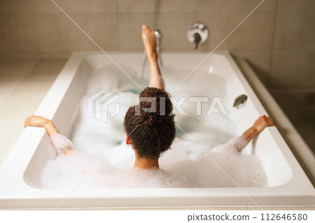 A woman is bathing in a bathroom tub filled with bubbles 112646580