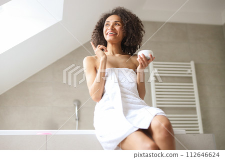 A woman, towel wrapped, sits on tub edge, revealing shoulder and thigh muscles A woman, towel wrapped, sits on tub edge, revealing shoulder and thigh muscles 112646624