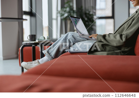 Person in comfort sitting on a couch using laptop near a window Person in comfort sitting on a couch using laptop near a window 112646648
