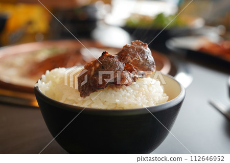 Rice and beef in a black bowl on a wooden table. 112646952