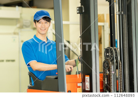 A man driving a forklift in a warehouse 112648893
