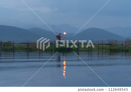 Burmese fisherman walking on bridge in Unle lake, natural river in Asia in Myanmar. People lifestyle. Burmese fisherman walking on bridge in Unle lake, natural river in Asia in Myanmar. People lifestyle. 112649543