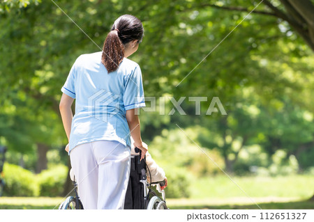 Senior woman in wheelchair and caregiver walking in the park Senior woman in wheelchair and caregiver walking in the park 112651327