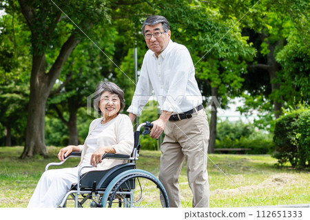 Senior couple walking in a wheelchair Senior couple walking in a wheelchair 112651333