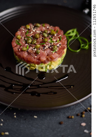 Tuna and avocado tartare with sesame seeds and capers on a dark ceramic plate Tuna and avocado tartare with sesame seeds and capers on a dark ceramic plate 112651746