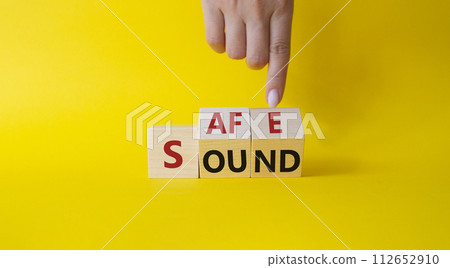 Safe and Sound symbol. Businessman hand points at cubes with words Safe and Sound. Beautiful yellow background. Business and Safe and Sound concept. Copy space Safe and Sound symbol. Businessman hand points at cubes with words Safe and Sound. Beautiful yellow background. Business and Safe and Sound concept. Copy space 112652910