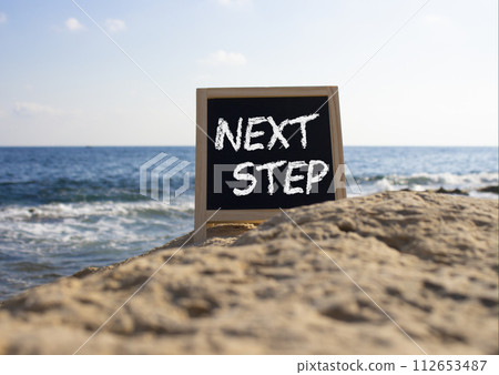 Next Step symbol. Concept words Next Step on black chalk background. Beautiful sea background. Business and Next Step concept. Copy space. Next Step symbol. Concept words Next Step on black chalk background. Beautiful sea background. Business and Next Step concept. Copy space. 112653487